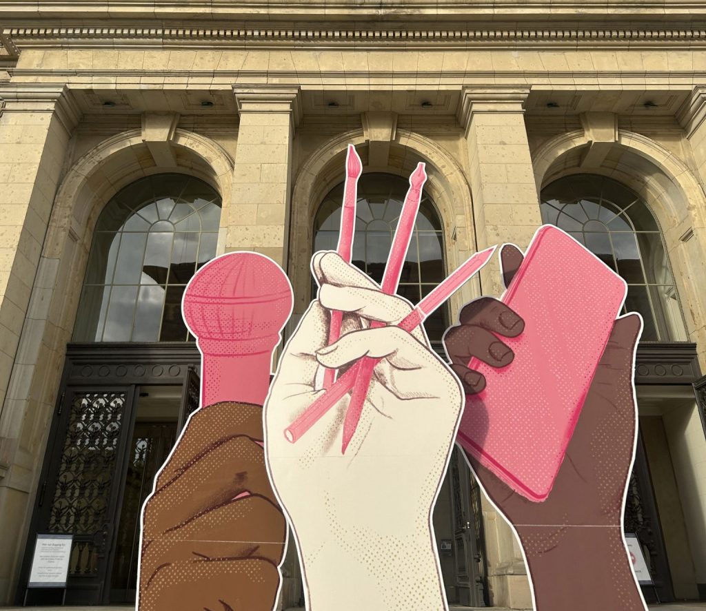 Foto vor dem Abgeordnetenhaus von Berlin. Vor dem Eingang stehen drei große Hände als Papp-Figuren. DIe linke Hand hält ein Mikrofon. Die mittlere Hand hält drei Stifte. Die rechte Hand hält ein Handy.